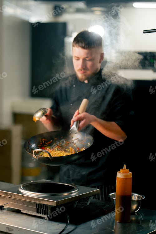 Preview: in professional kitchen the chef prepares wog noodles with vegetables on a large frying pan