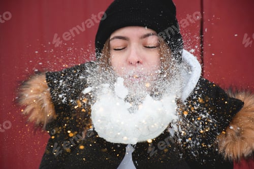 Preview: Young teenage girl blowing snow with glitter and sparkles from against red background