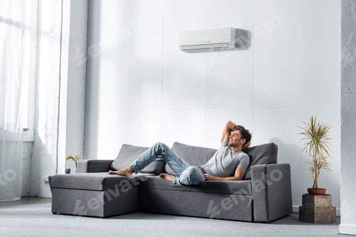 Preview: handsome and smiling man in jeans and t-shirt lying on sofa