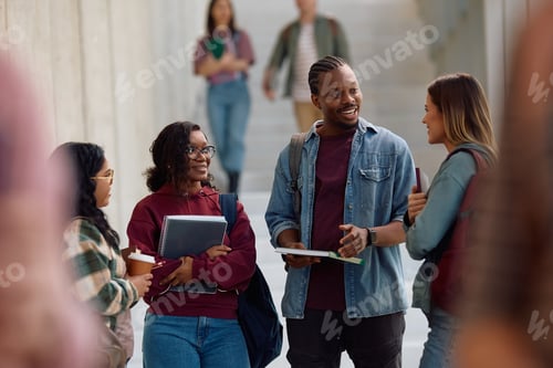 Preview: Happy college friends talking while standing in a hallway.