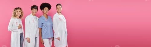 Preview: smiling multiethnic doctors with ribbons on coats standing isolated on pink, banner, breast cancer