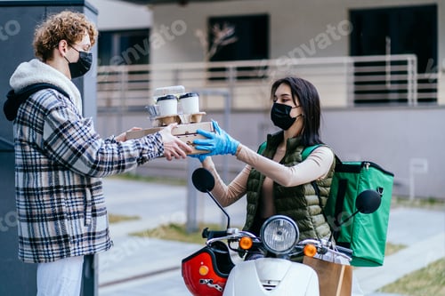 Preview: Young female courier delivering food on a scooter, giving order for a man in protective mask