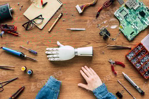 Preview: cropped image of man with amputee sitting at table with prosthetic arm surrounded by tools