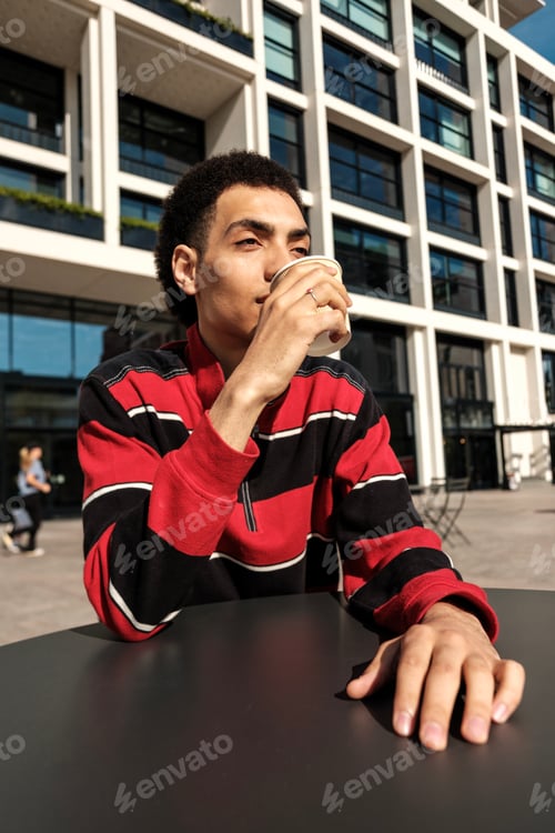 Preview: Young man drinking coffee from paper cup in urban setting