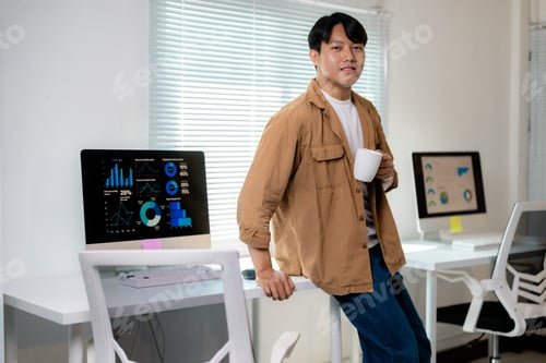 Preview: Young entrepreneur analyzing graphs and drinking coffee during a break in the office