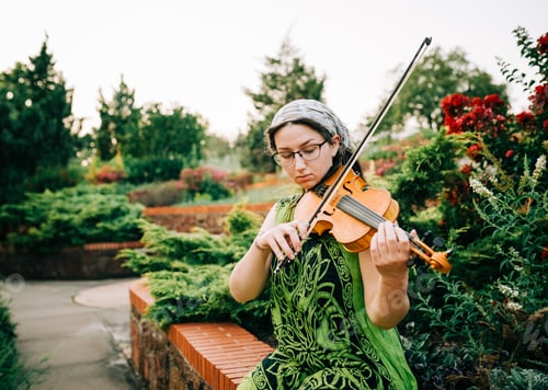 Preview: A young woman playing the violin outside on a summer day in a lovely green garden.