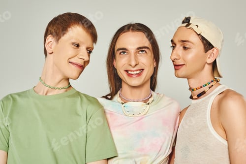 Preview: portrait of three lgbtq people with colorful beads smiling while standing together on grey