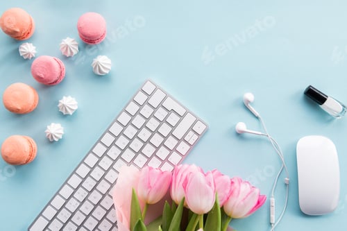 Preview: top view of keyboard, macarons, nail polish, earphones and bouquet of flowers isolated on blue