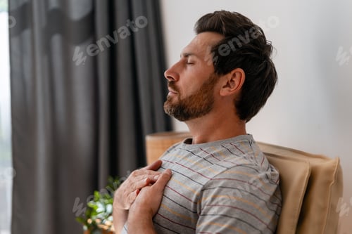 Preview: Man practicing mindfulness breathing with hands on chest at home