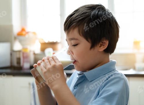 Preview: school boy drinking glass of milk for breakfast, Happy child standing in kitchen drinking warm milk