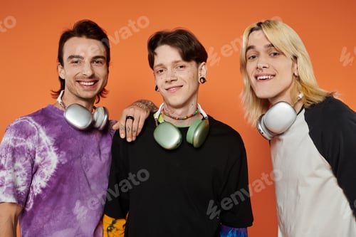 Preview: Queer friends pose with headphones against orange background