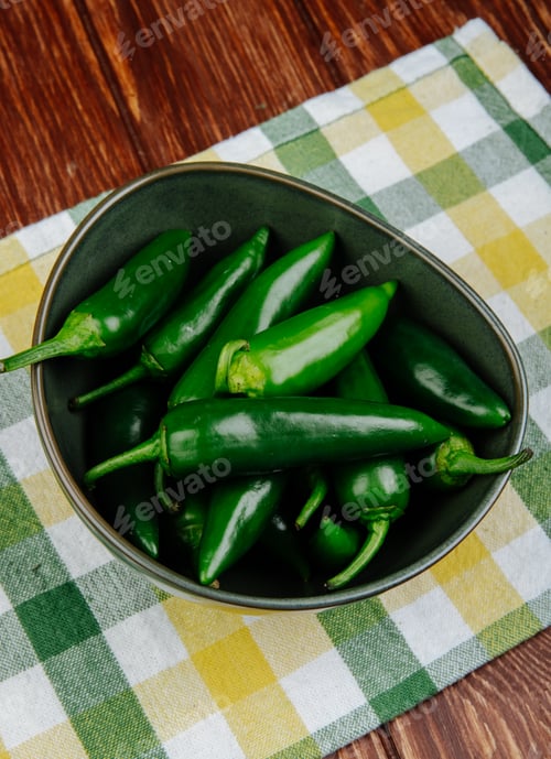Preview: side view of fresh green chili peppers in a bowl on plaid napkin on wooden rustic background