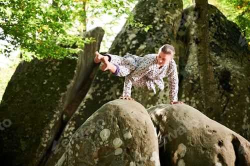 Preview: Woman practicing yoga outdoors in forest. Barefoot female on yoga mat surrounded by trees and rocks