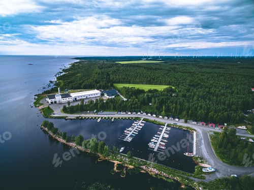 Preview: Aerial view of nordic summer landscape with blue sea and green forest with windmills on the horizon.