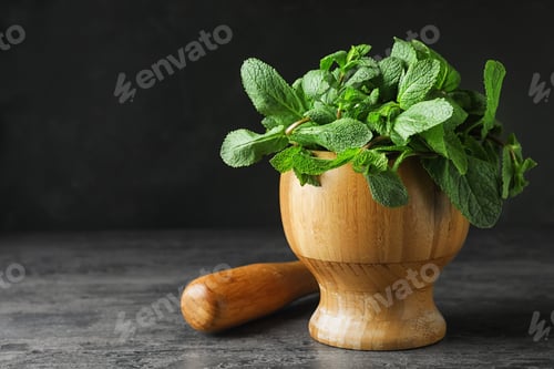 Preview: Wooden mortar full of fresh green mint on grey table against dark background