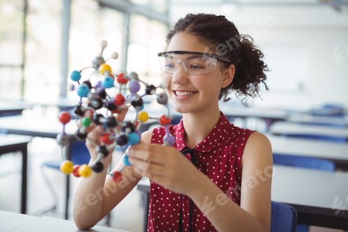 Preview: Happy schoolgirl holding experimenting model in laboratory