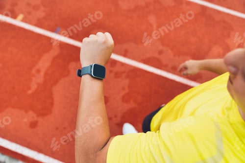 Preview: Male runner using smartwatch to track workout progress on the running track