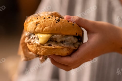 Preview: Customer holding a delicious cheeseburger with melting cheese and sesame seeds