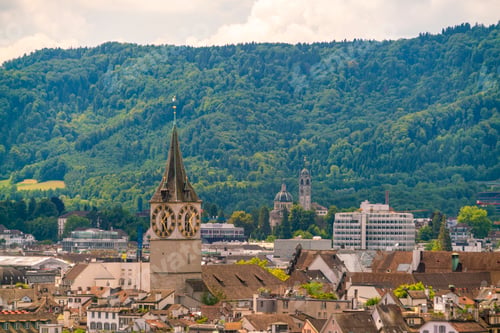 Preview: Scenic view of a historic town with a clock tower and green hills in the background.
