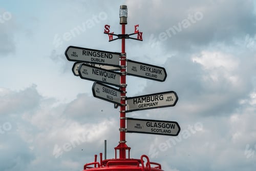 Preview: Red sign pole with compass directions showing ways to multiple big cities around the world