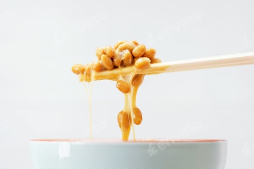 Preview: Wooden chopsticks holding japanese natto beans on gray background.