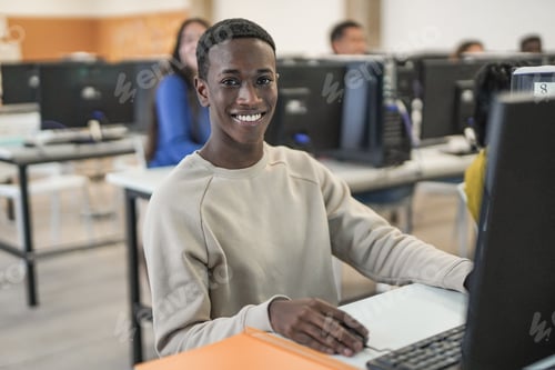 Preview: Young african boy smiling on camera inside computer class room