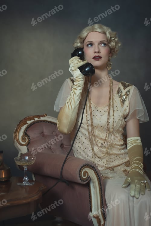 Preview: Retro 1920S Fashion Woman On The Phone While Sitting On Sofa Beside Table With Glass Of Champagne.