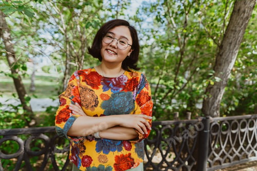 Preview: Smiling female with crossed arms standing in a lush park, exuding happiness