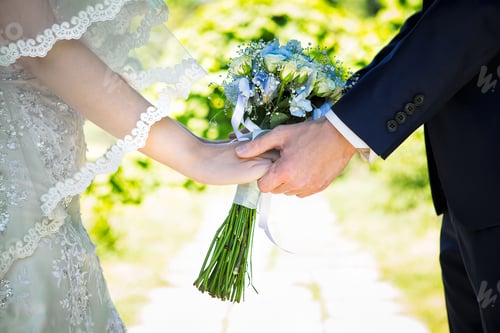 Preview: Hands of loving couple holding a wedding bouquet of white roses flowers