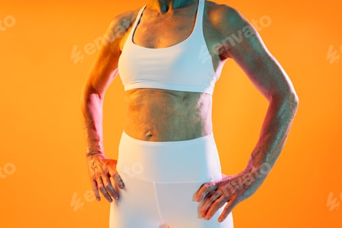 Preview: Senior fitness woman showing toned body after workout on orange background