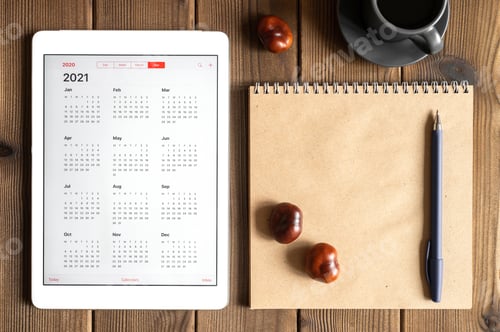Preview: tablet with calendar for 2021, a cup of coffee and a craft paper notebook on a wooden background