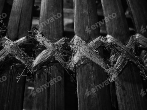 Preview: Closeup grayscale of a deteriorated wooden fence: a chair made of bamboo tied with raffia