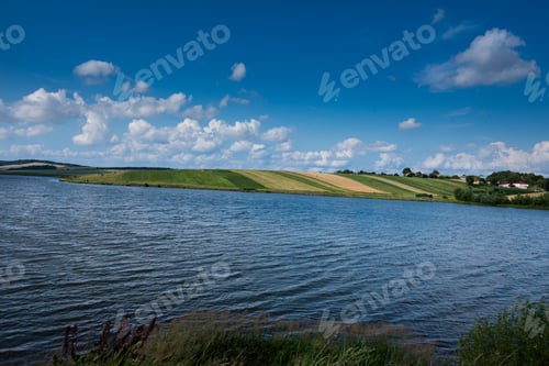 Preview: reservoir, hills fields under a bright blue sky with clouds