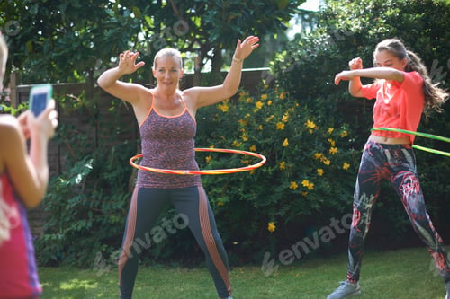 Preview: Girl photographing mother and teenage sister hoola hooping in garden