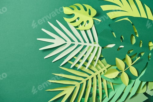 Preview: top view of tropical paper cut palm leaves on green background with copy space