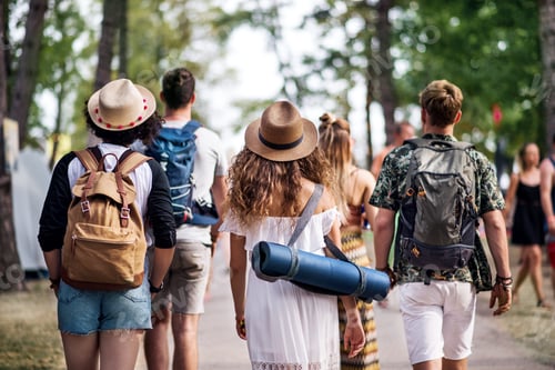Preview: Rear view of group of young friends with backpack walking at summer festival.