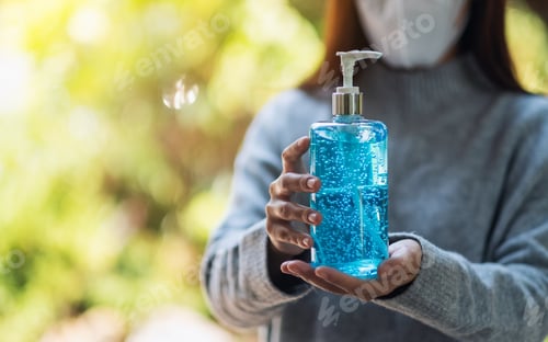 Vista previa: a woman wearing protective mask holding and showing a bottle of alcohol gel sanitizer