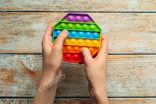 Preview: Woman using pop it fidget toy at light wooden table, top view