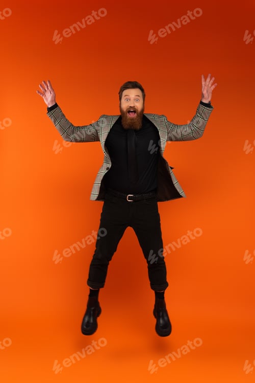 Preview: Astonished bearded man in blazer jumping on red background