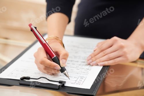 Preview: Woman Signing Document with Red Pen in Office
