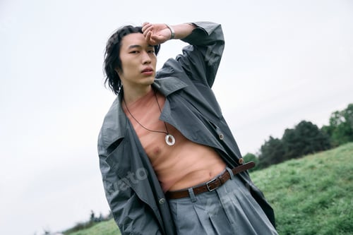 Preview: Stylish young man showcasing fashion in a serene park setting during a cloudy day