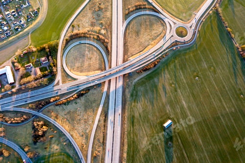 Preview: Aerial top view of modern highway road intersection, house roofs on spring green field background