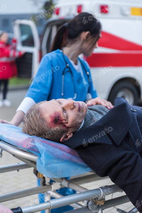 Preview: female doctor moving wounded mature man on ambulance stretcher
