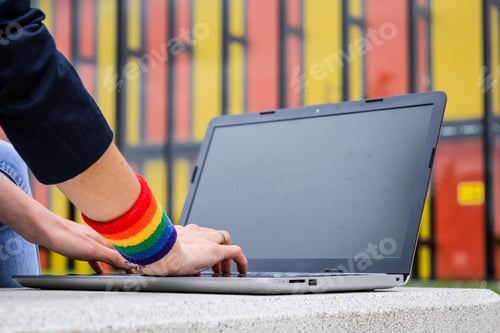 Preview: Close-up of woman hands with laptop and LGBT bracelet in modern park . LGBTQIA culture.