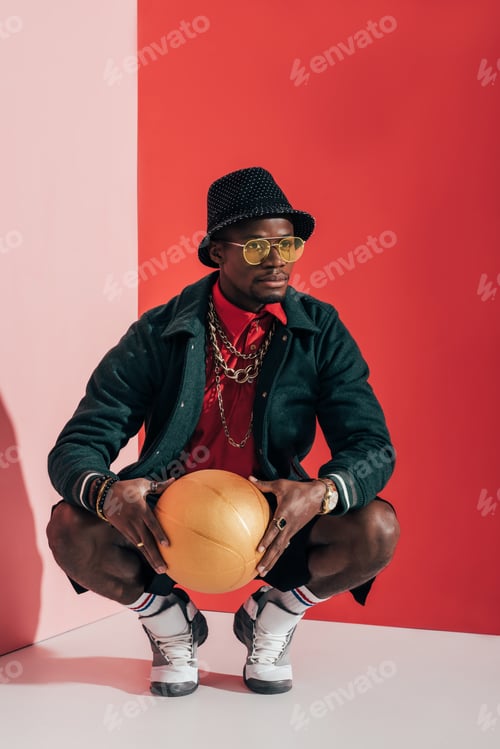 Preview: handsome stylish african american man with golden basketball ball crouching and looking away