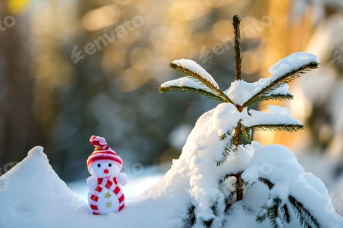Preview: Small funny toy baby snowman in knitted hat and scarf in deep snow outdoors