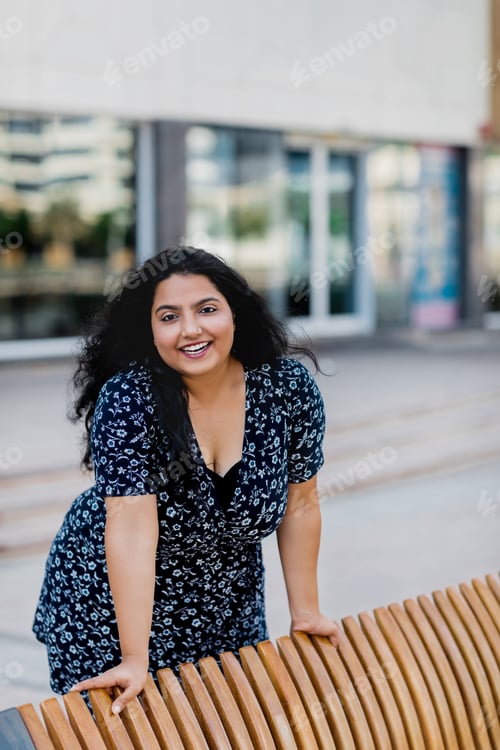 Preview: A charming Indian woman stands by the bench and smiles.