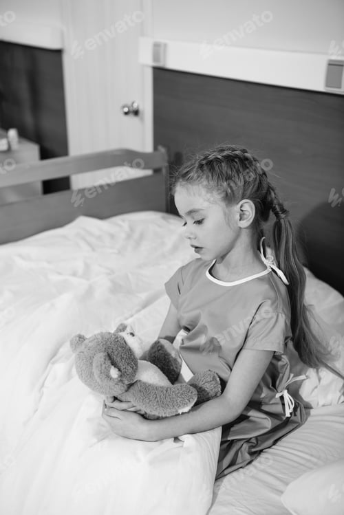 Preview: Serious little girl with teddy bear sitting on hospital bed, black and white photo