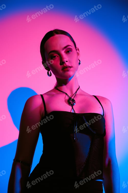 Preview: Captivating young woman poses in stylish outfit against a vibrant pink and blue backdrop