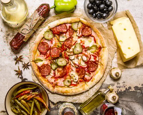 Meat pizza with ingredients around cheese, pepperoni, meat, olives, peppers, mushrooms and spices.